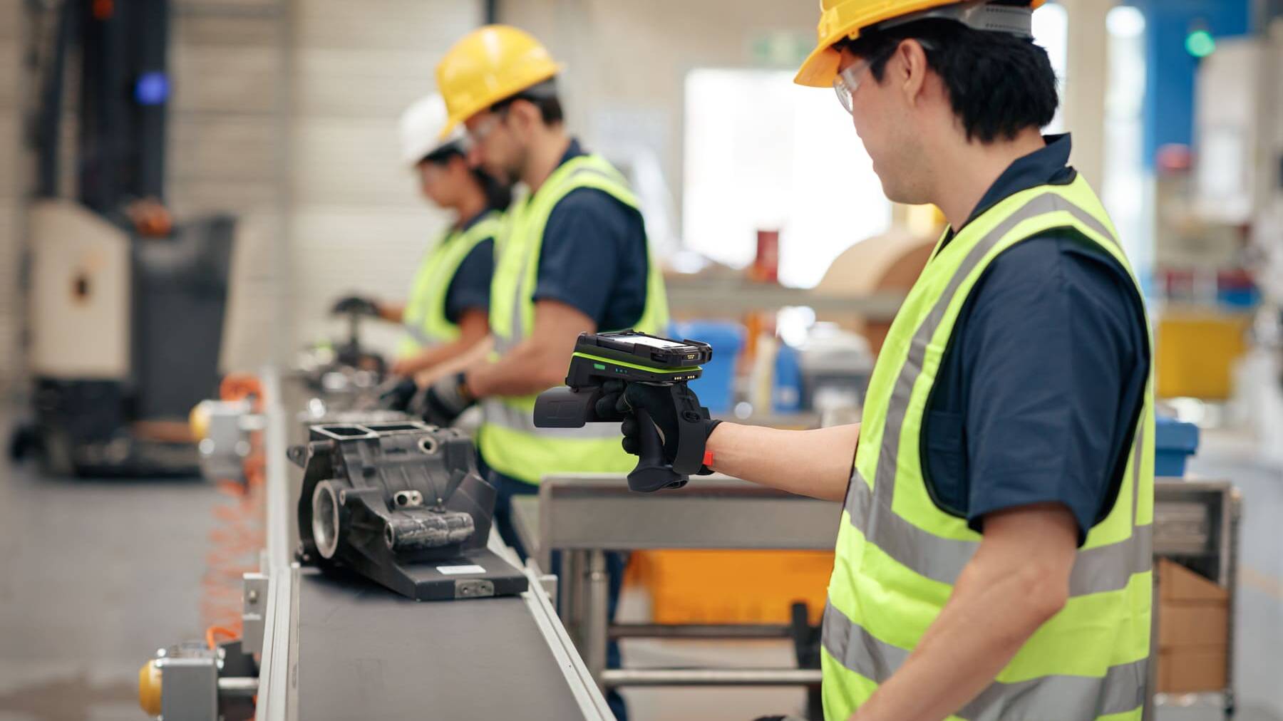Opérateurs logistiques équipés de gilets de sécurité utilisant un lecteur RFID en atelier.