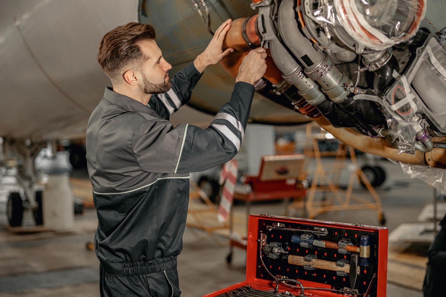 Technicien a&eacute;ronautique intervenant sous un avion avec une caisse &agrave; outils, illustrant le suivi outillage RFID et la pr&eacute;vention FOD